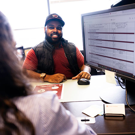 A black male advisor shares a major map on his computer screen with a student. 