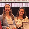 Two white, female advisors are holding award plaques and smiling at the camera. 