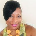 Latecia is pictured from the neck up. She has brown skin, brown eyes, and short black hair. She is smiling. 
