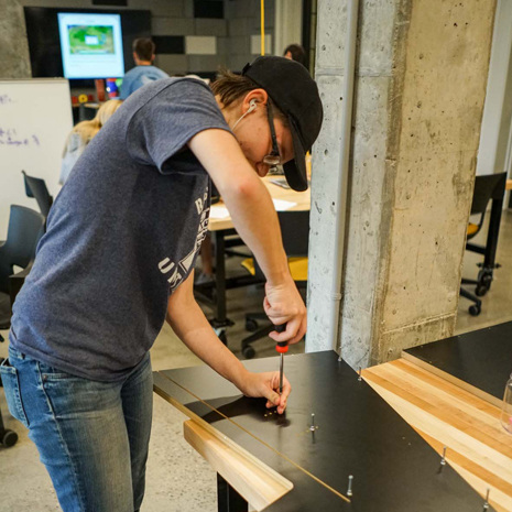 A person is screwing screws into the side of a gaming cabinet in the Rhodos Fellows makers space