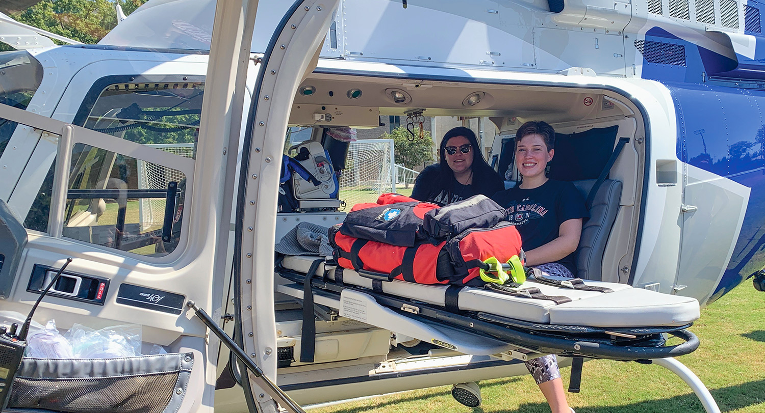 Zola Jane and another student sits in a helicopter holding and empty stretcher.