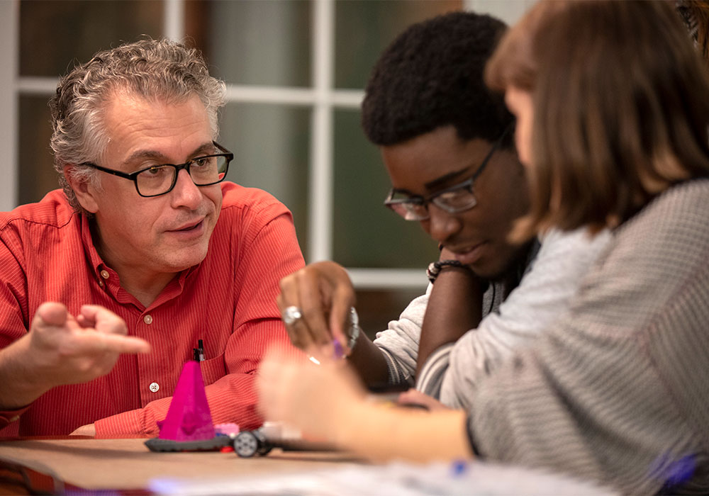 Professor talking to two students who are building a robot with legos.