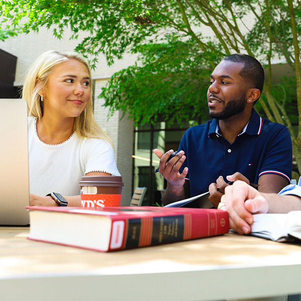 Students in an outdoor courtyard table talking with law books and a laptop.