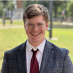 man smiling outside with garnet tie on and gray blazer