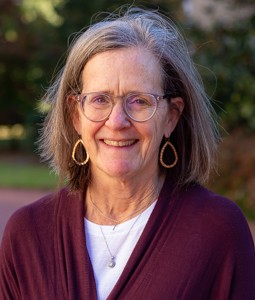 a woman smiling with glasses on outside and a garnet sweater on