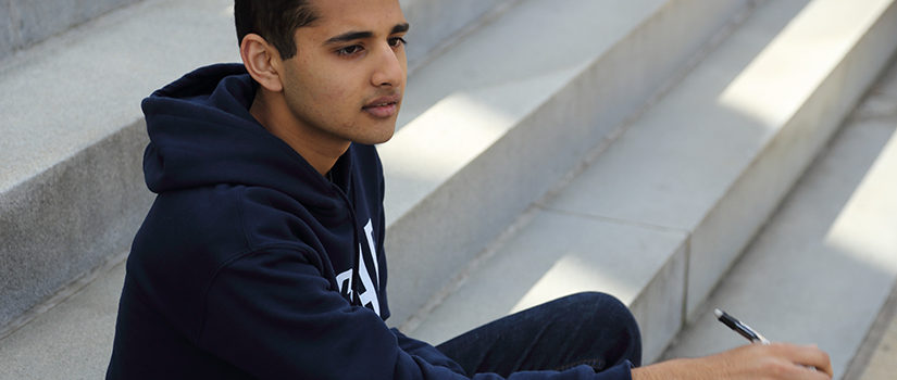 Student sitting on stairs with pen and paper in hand