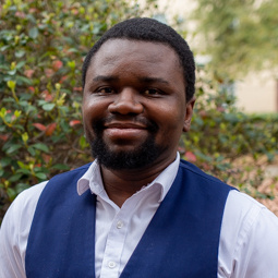 man with a blue vest on smiling outside