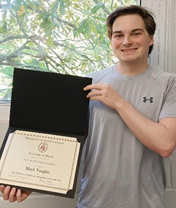 photo of a man in a gray tshirt holding up an award. 