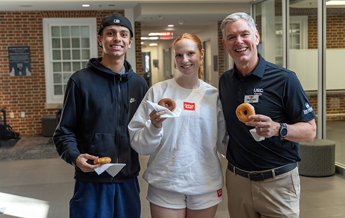 the dean and a male and female student holding donuts