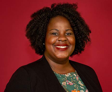 Mamee Groves gives a warm smile in this headshot where she is pictured on a garnet background