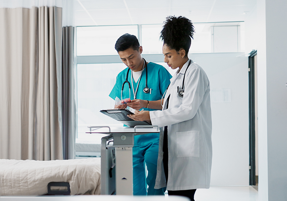 A doctor and nurse review a chart together in a hospital room
