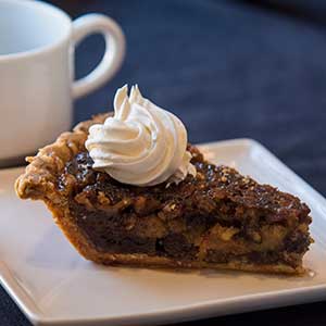 Slice of pie on a white plate and a cup of coffee sit on a blue table cloth. 