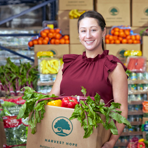 Erinn Rowe smiles and holds a box of food. There are other food items in boxes and on shelves around her.