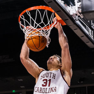 Man in garnet and while basketball jersey with South Carolina on it dunks a basketball