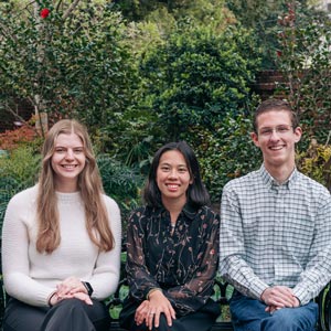 three people sit on a bench in a garden setting